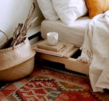 Yatağın üzerinde rahat çarşaf ve pikeler, yanda kitaplar ve yerde el dokuma kilim